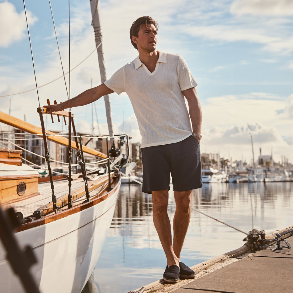 FRONT FULL BODY EDITORIAL IMAGE OF MODEL BY THE WATER WEARING ETANNE POLO SHIRT AND ARCHER SHORTS